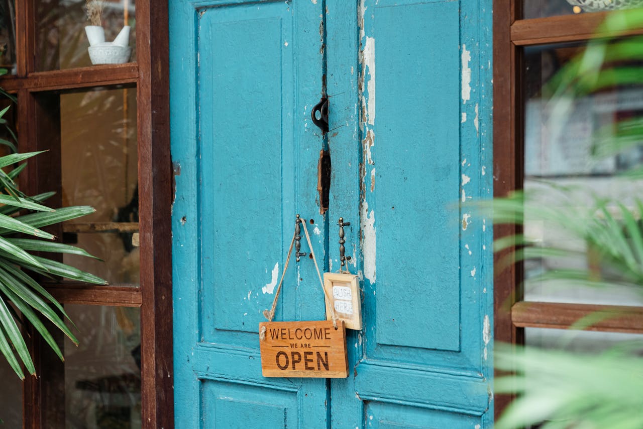 A rustic blue door with a wooden welcome sign showcasing an open establishment.
